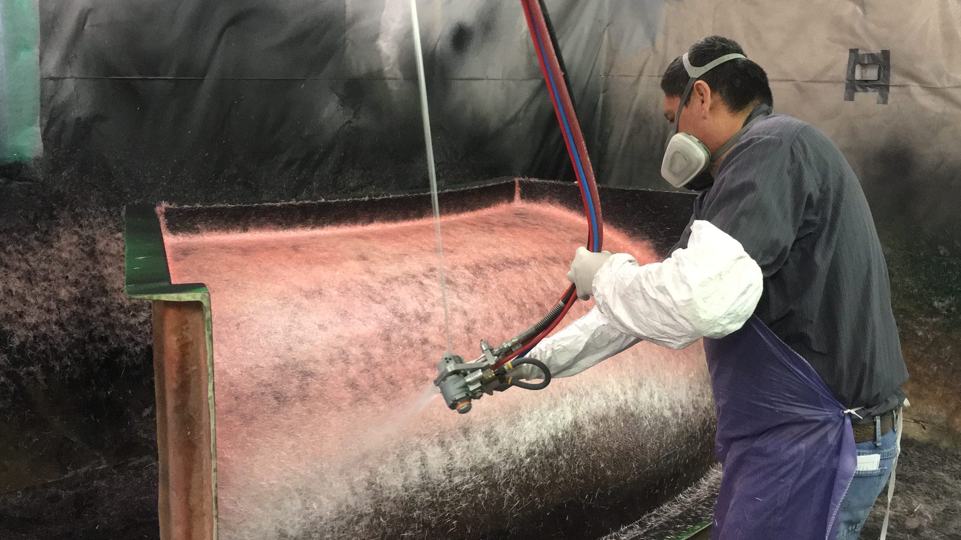 Technician applying chopped fiberglass to a large mold